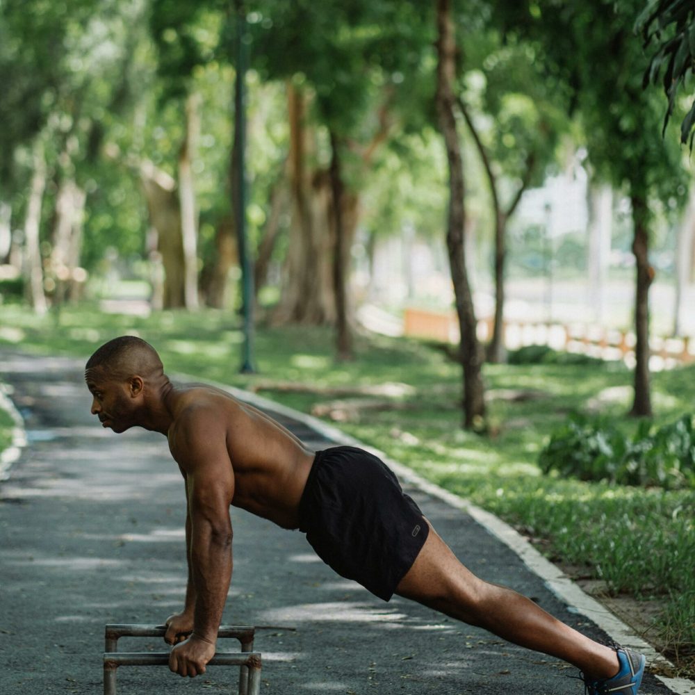 pexels-photo-4803930-4803930 Shirtless man in black shorts doing push-ups on parallel dip bars in park.